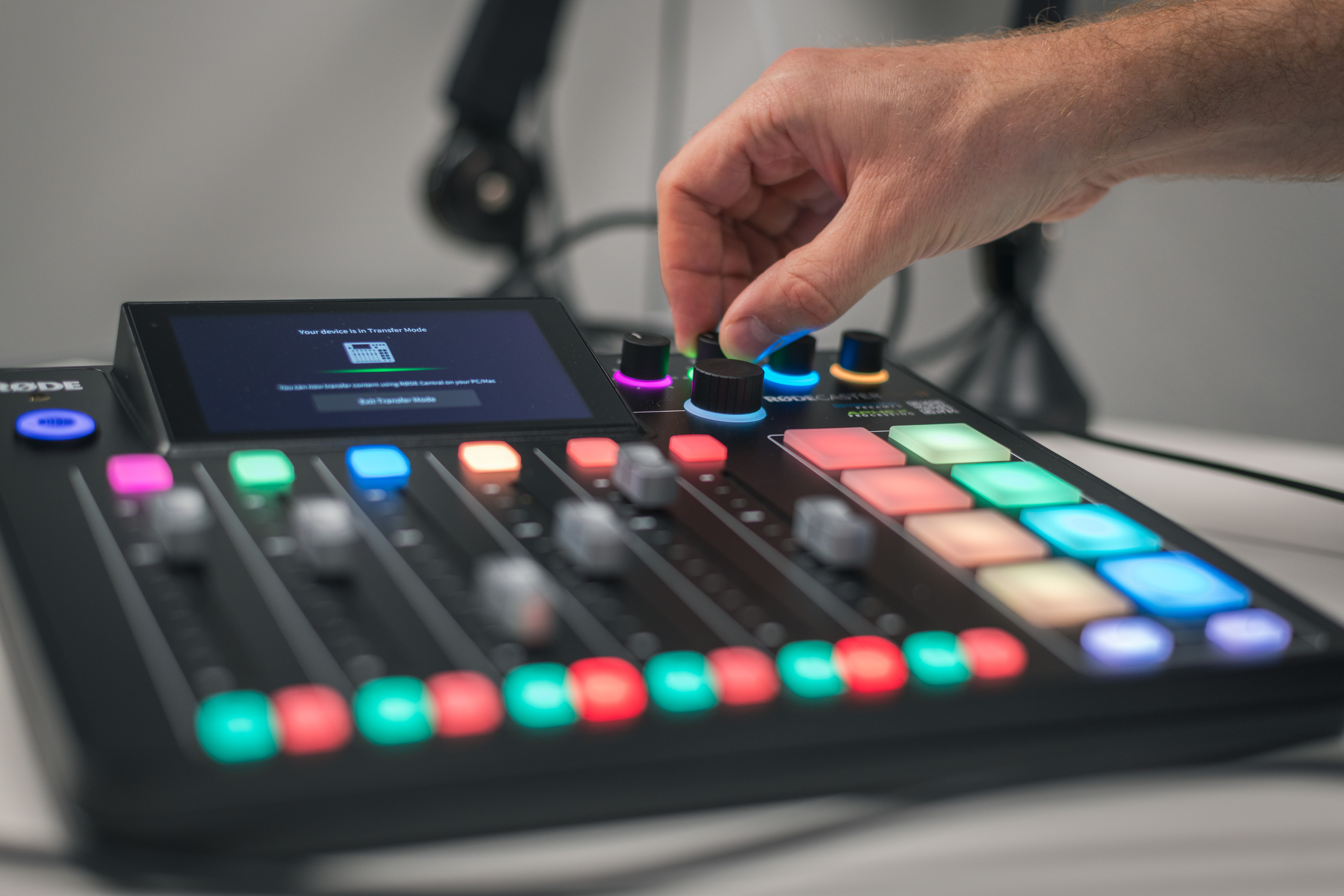 A man's hand twisting a dial on a sound board. The buttons on the sound board are colorful. No faces. 