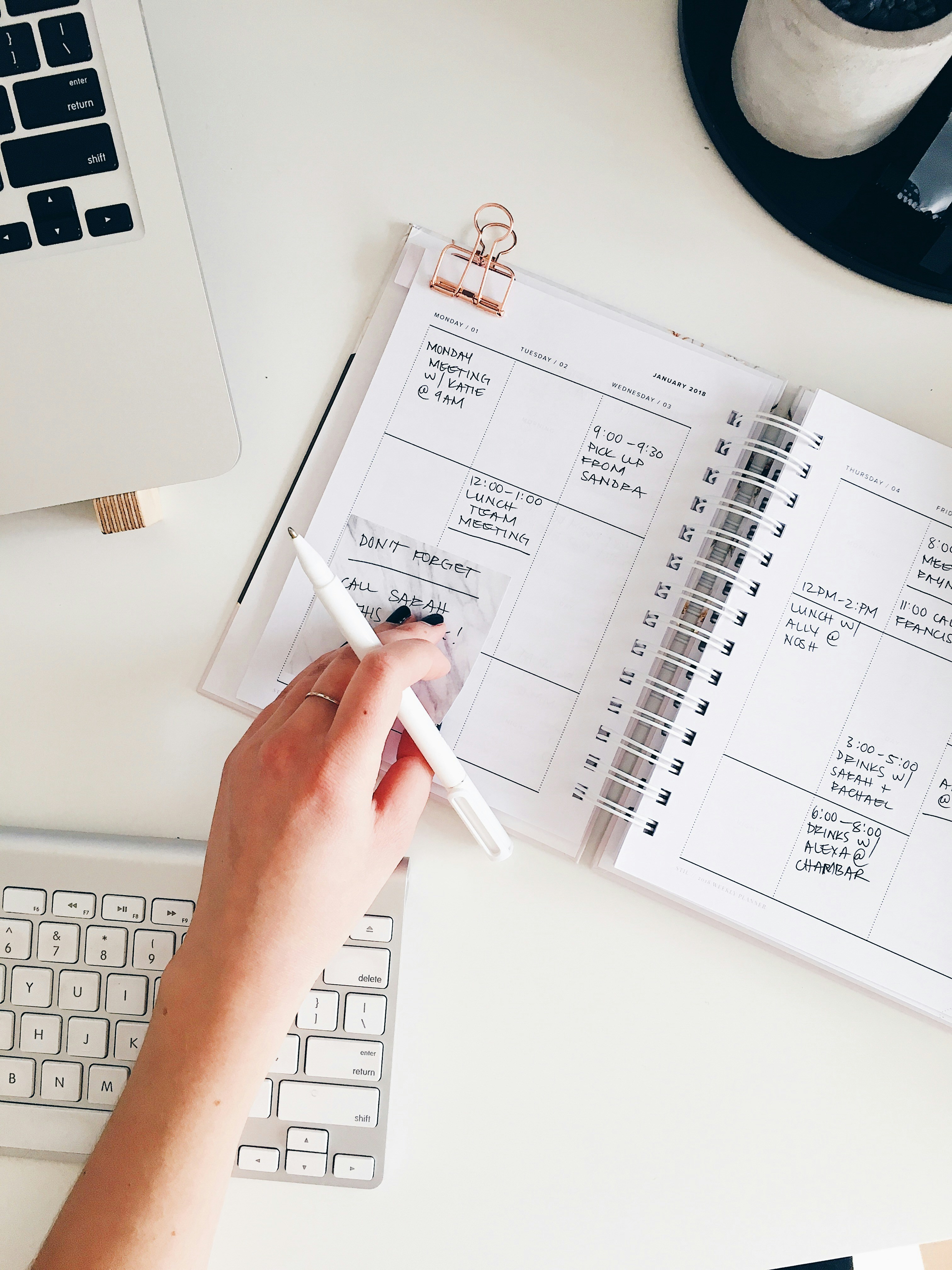 a young woman's hand writing in her planner with a Mac keyboard 