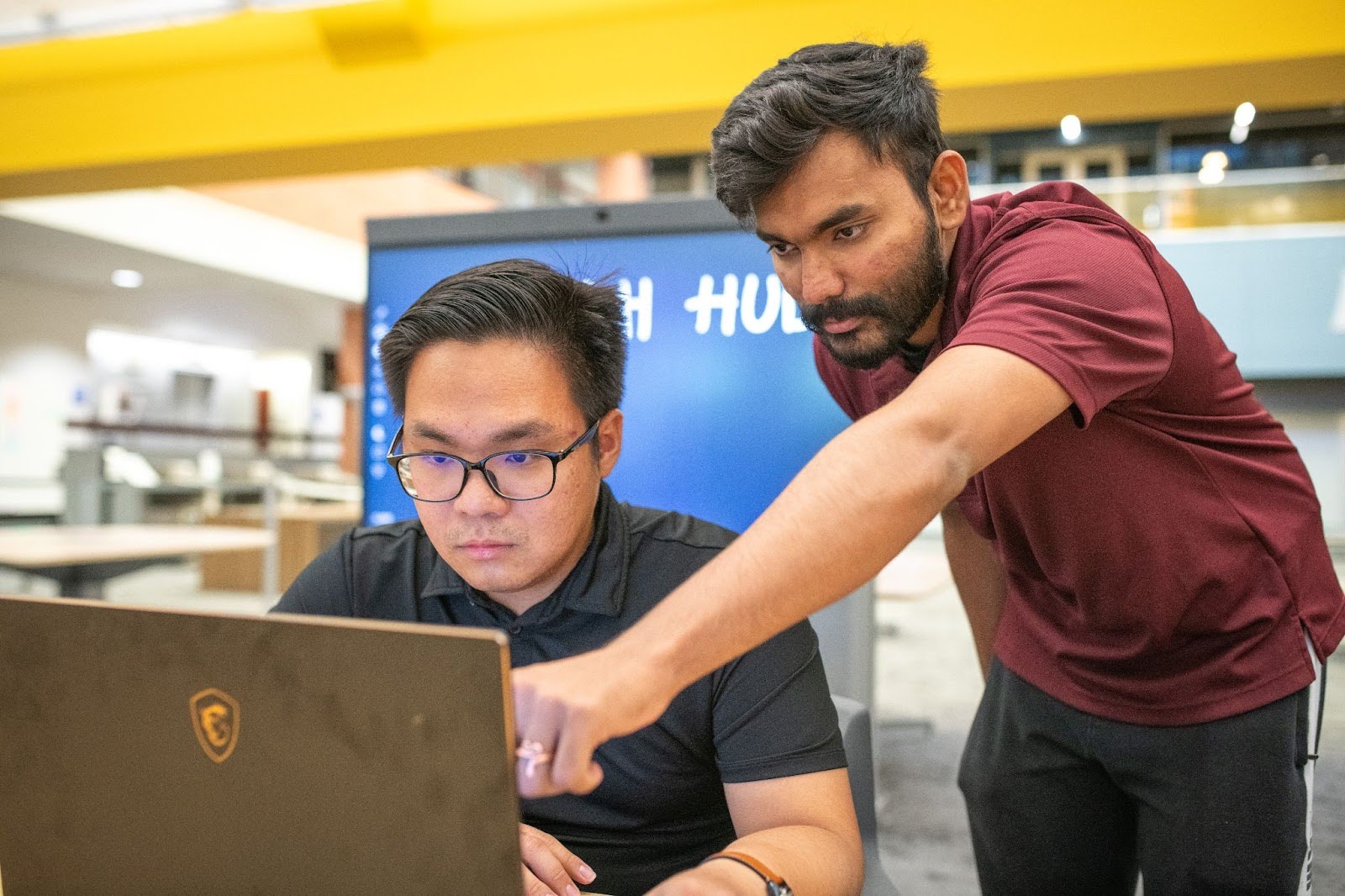 A Tech Hub employee assists a student on a laptop.