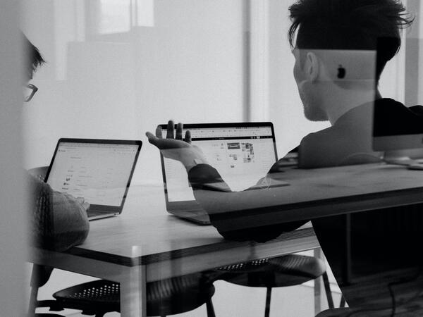 black and white image of two people working at laptops having a discussion and collaborating 