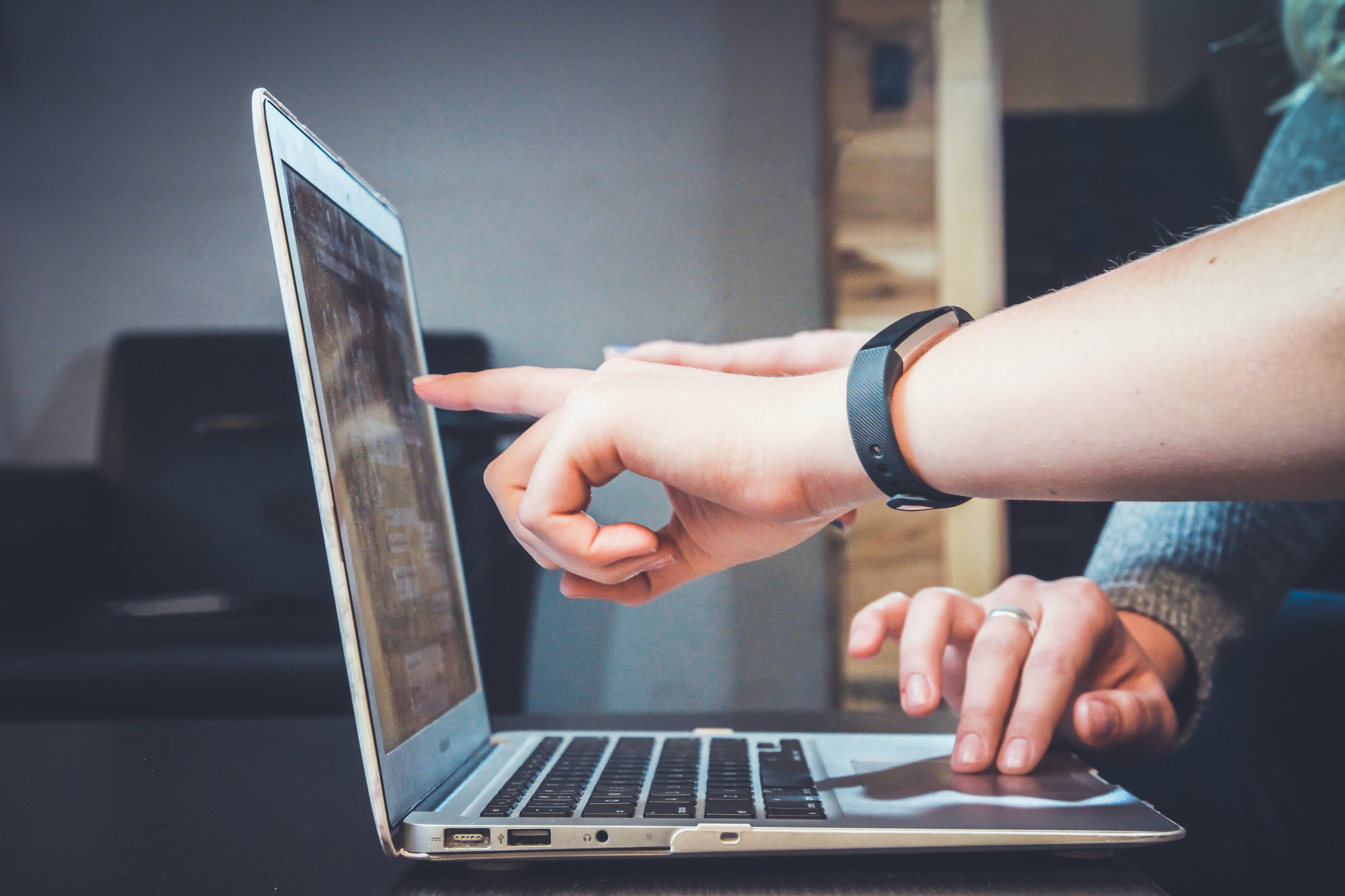 Someone points at a laptop screen while someone else is typing 