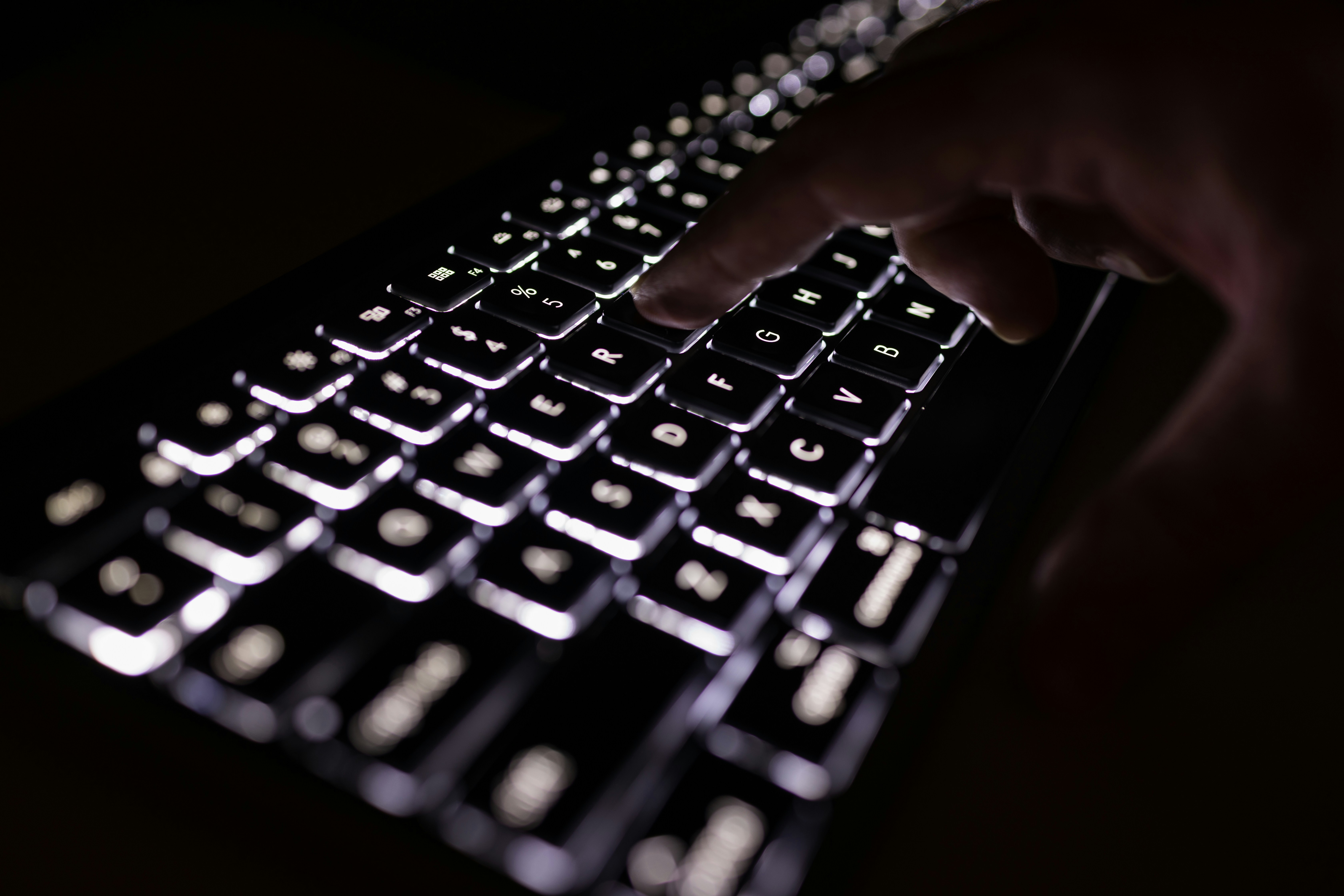 Someone typing on a black keyboard that is backlit with white light