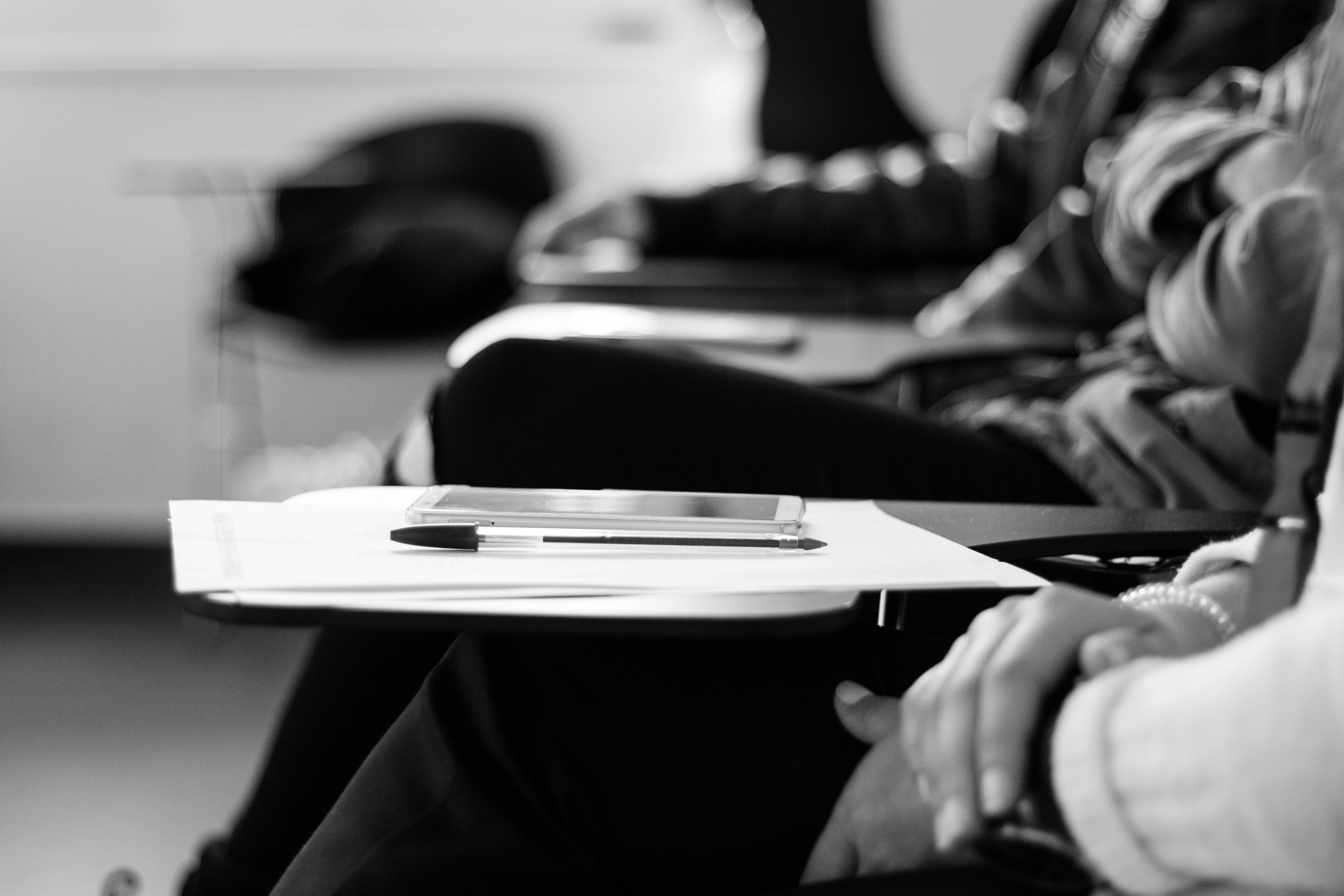 Black and white photo with no faces of students in a lecture hall. 